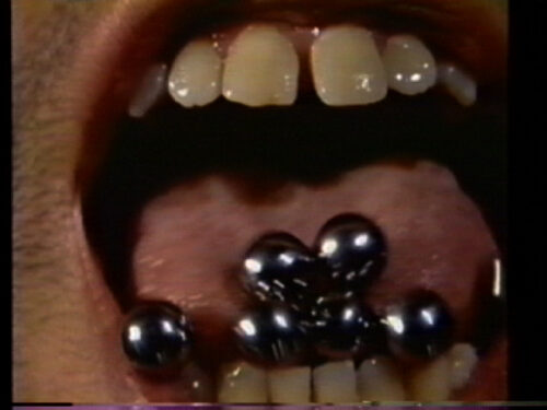 Video still of a mouth open wide with marbles falling out of the mouth